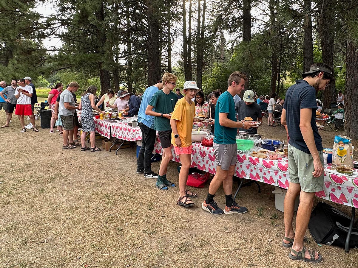 Large group of people getting food outside on tables